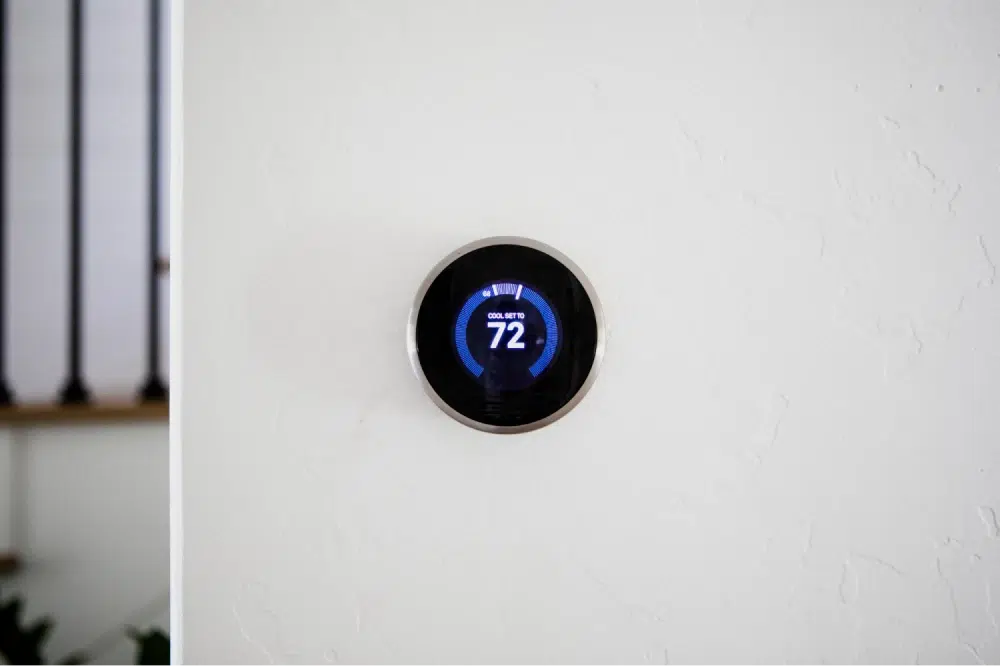 Smart thermostat on a white wall displaying a cool set temperature of 72 degrees.