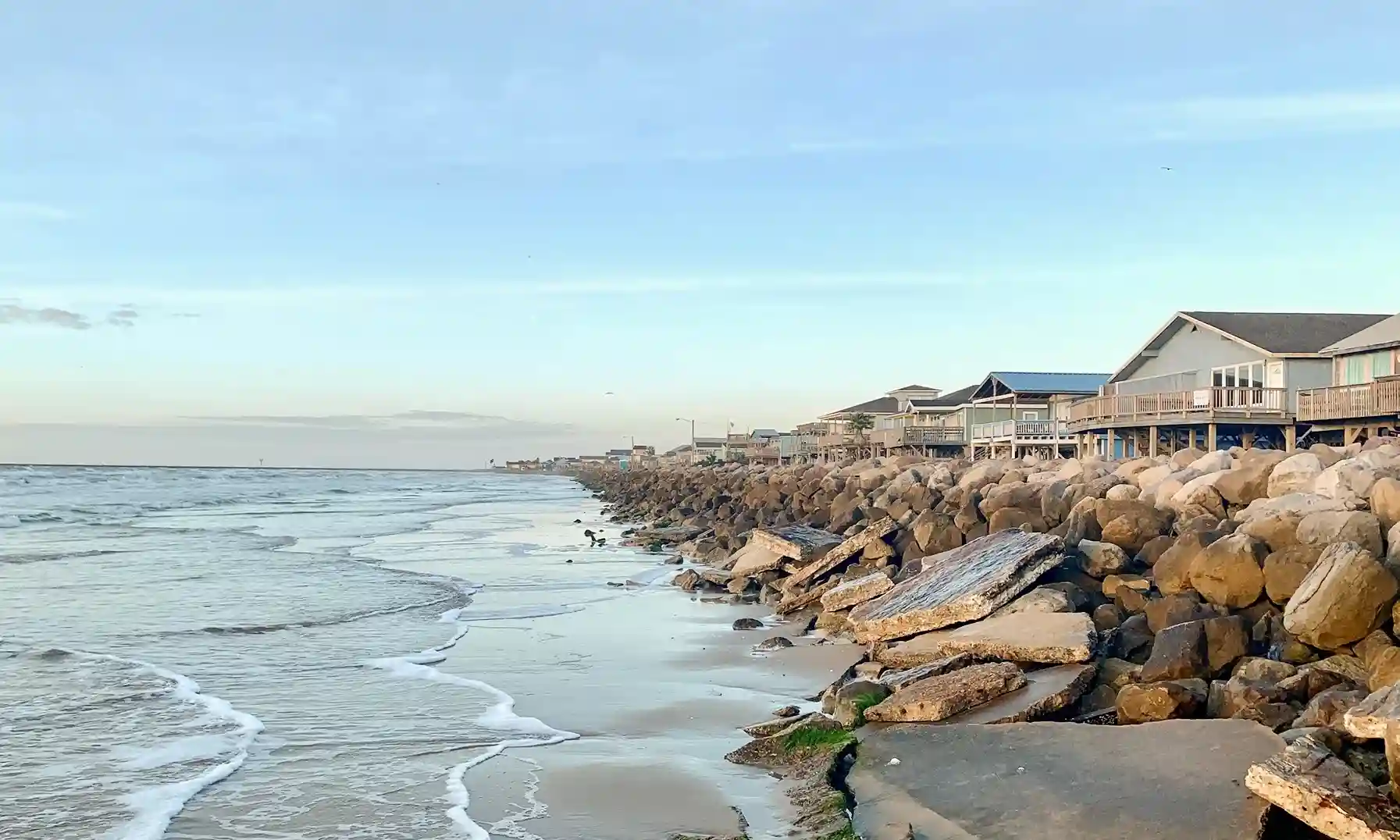 Seashore with rocky barrier beside beachfront homes during low tide at dusk - things to do south texas