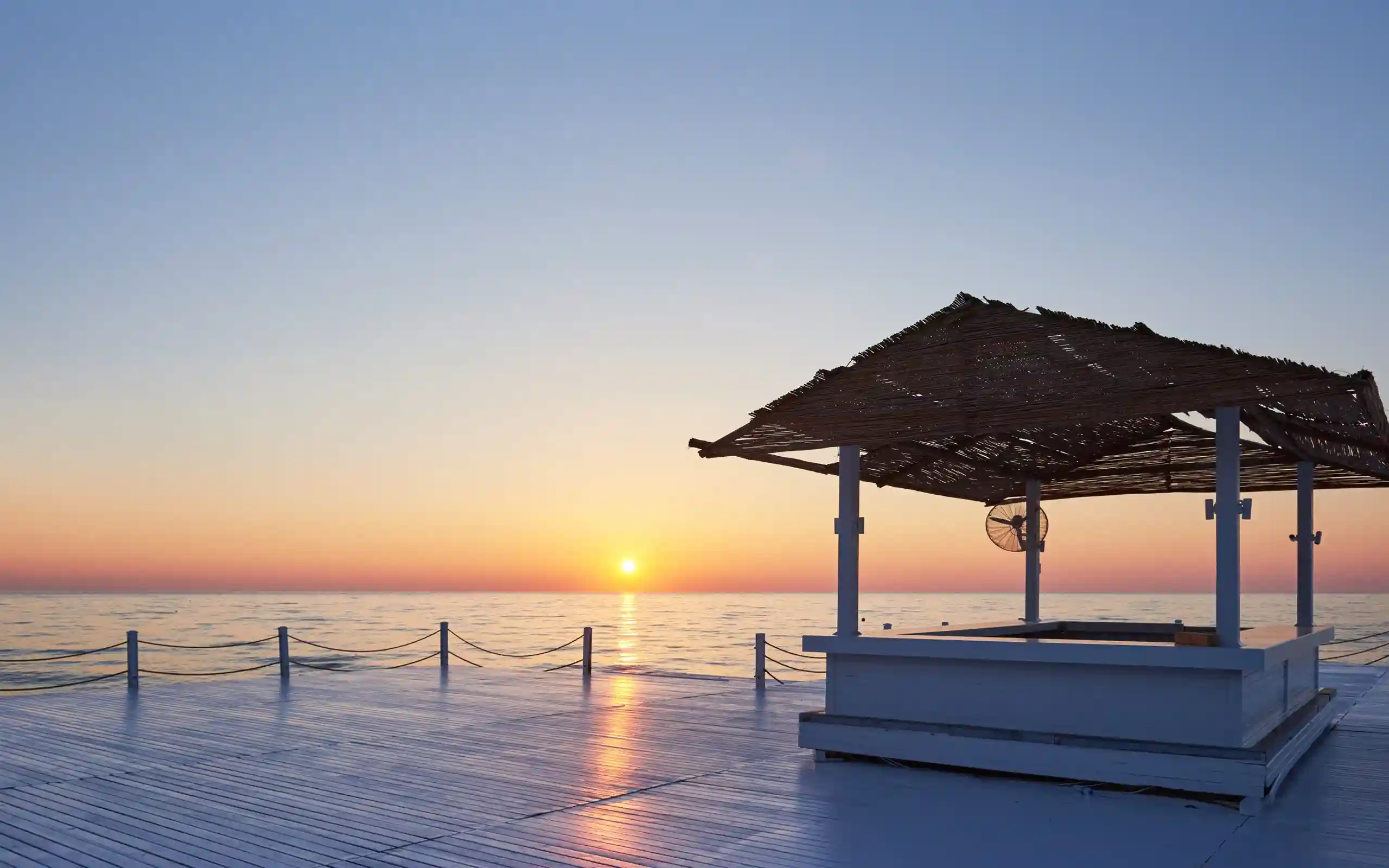 Sunset over the ocean viewed from a wooden deck with a thatched roof structure - things to do south texas